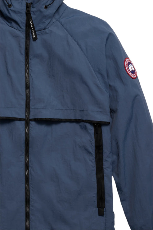Close-up of a blue hooded jacket with a visible logo patch on the sleeve and a black zipper.