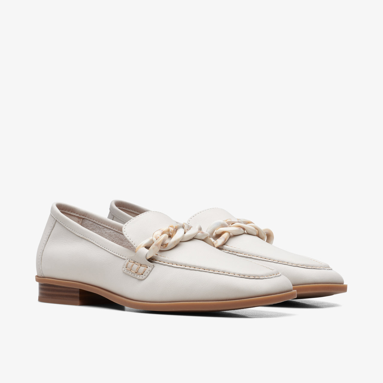 A pair of off-white loafers with chain embellishments, light brown soles.