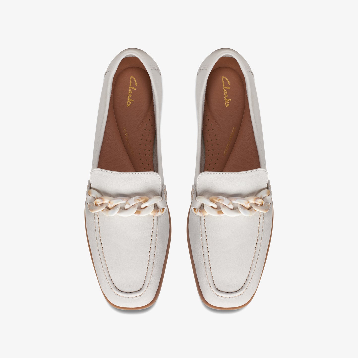 Overhead view of two white leather loafers with a chain detail.