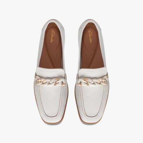 Overhead view of two white leather loafers with a chain detail.