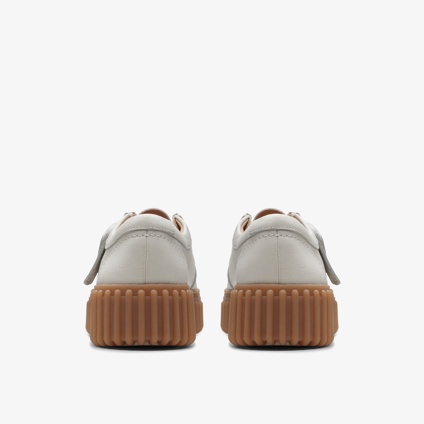 Pair of white casual shoes with thick brown treaded soles, shown from the back.