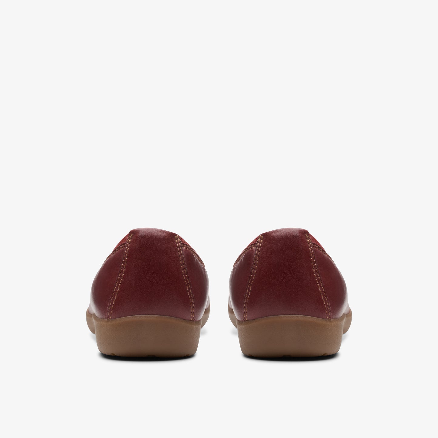 Back view of a pair of red leather ballet flats with brown soles.