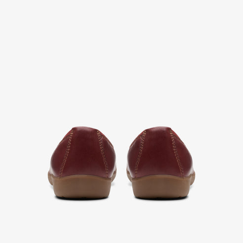 Back view of a pair of red leather ballet flats with brown soles.