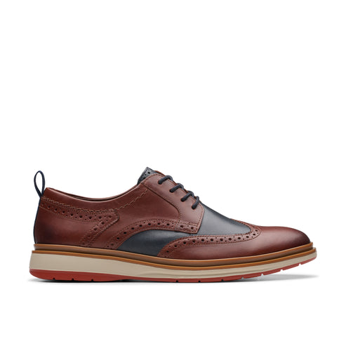 Brown leather wingtip dress shoe with black accents and a red and white sole.