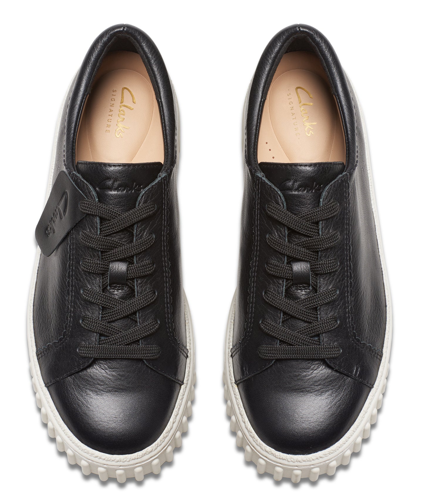 Overhead view of a pair of black leather sneakers with white soles and black laces; a tag with text is attached to the left shoe.