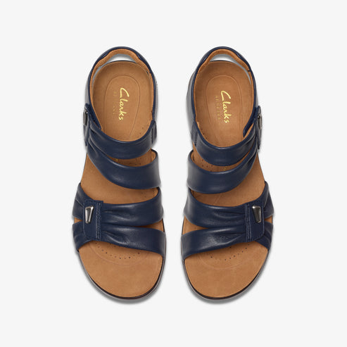 Overhead view of two navy blue leather sandals with two straps and a silver buckle. "Clarks Artisan" is printed on the inner sole.