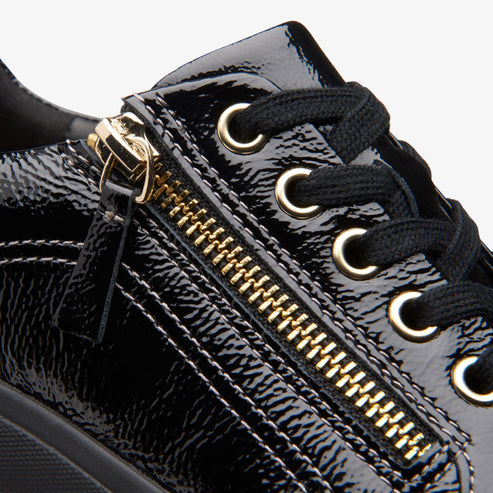 Close-up of black patent leather shoe featuring gold zipper and black laces.