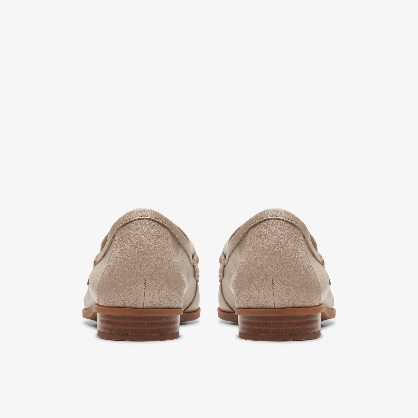 A pair of closed-back taupe loafers with brown soles are viewed from behind.