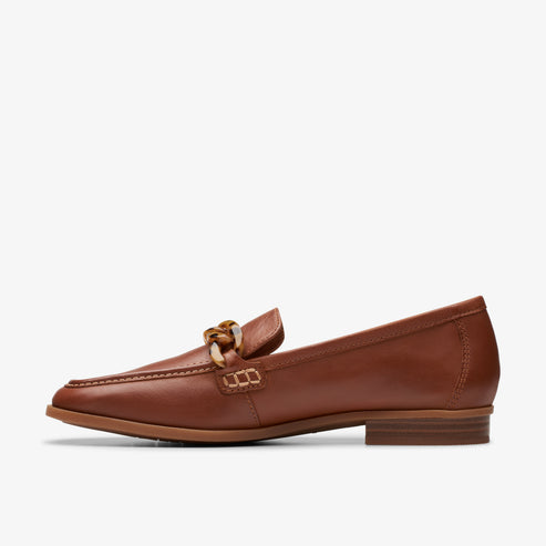 A brown leather loafer with a gold chain embellishment.