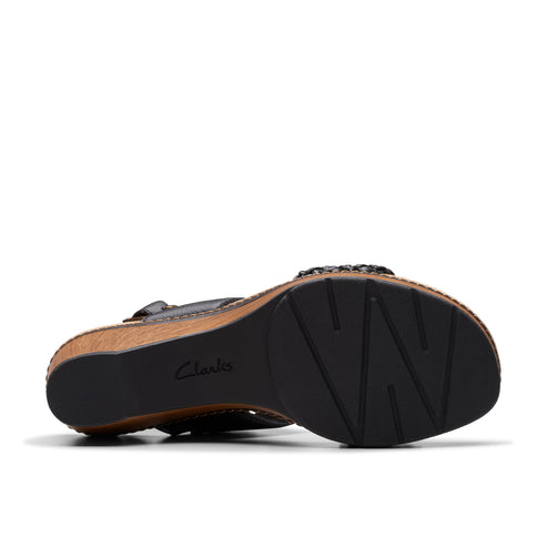 Bottom view of a black wedge sandal showing a dark, patterned sole.