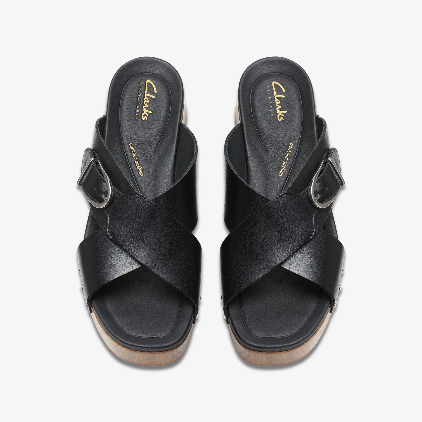 Overhead view of two black leather slide sandals with buckle, on a wooden sole. "Clarks signature" text is visible on the inner sole.
