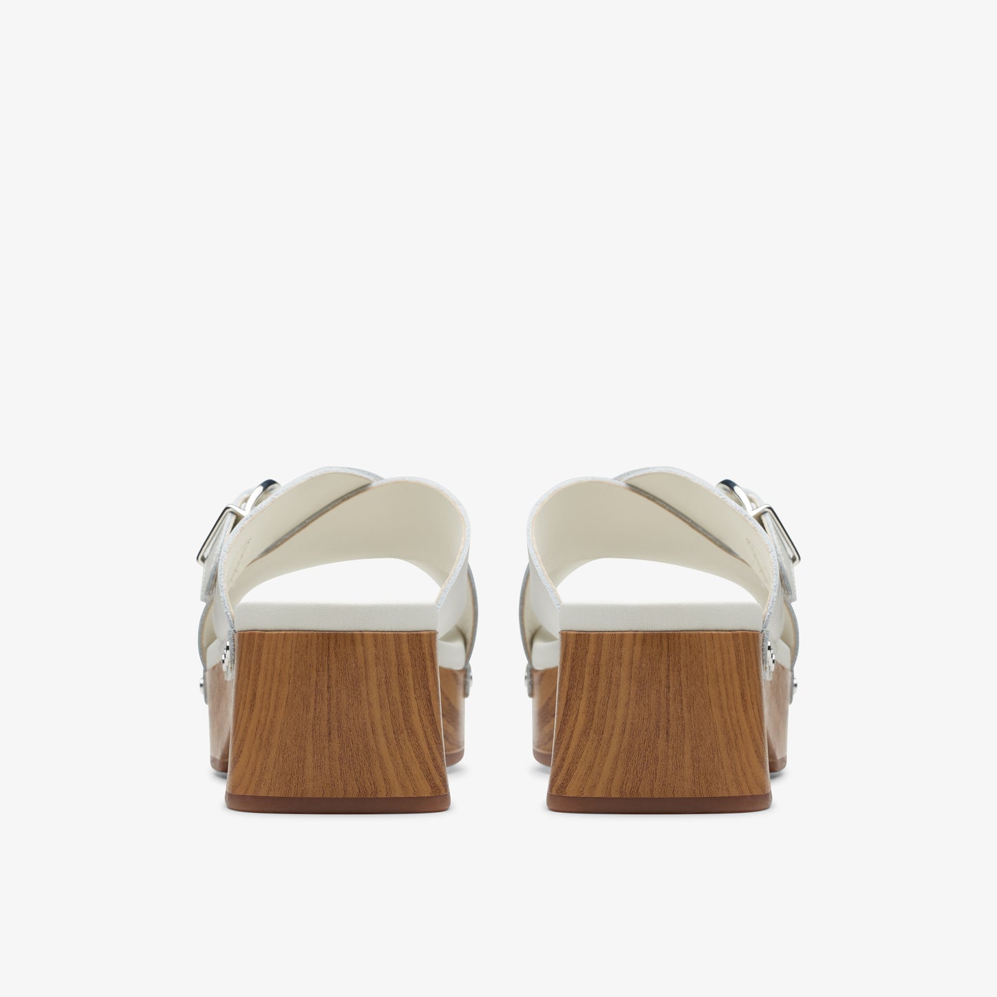 Pair of silver, block-heeled sandals with criss-cross straps and silver buckles; heels have a wood grain finish.