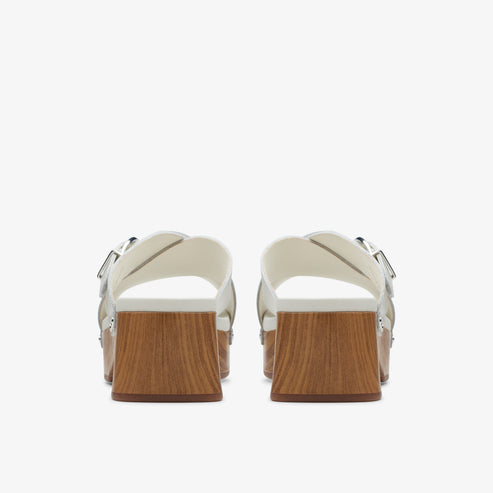 Pair of silver, block-heeled sandals with criss-cross straps and silver buckles; heels have a wood grain finish.