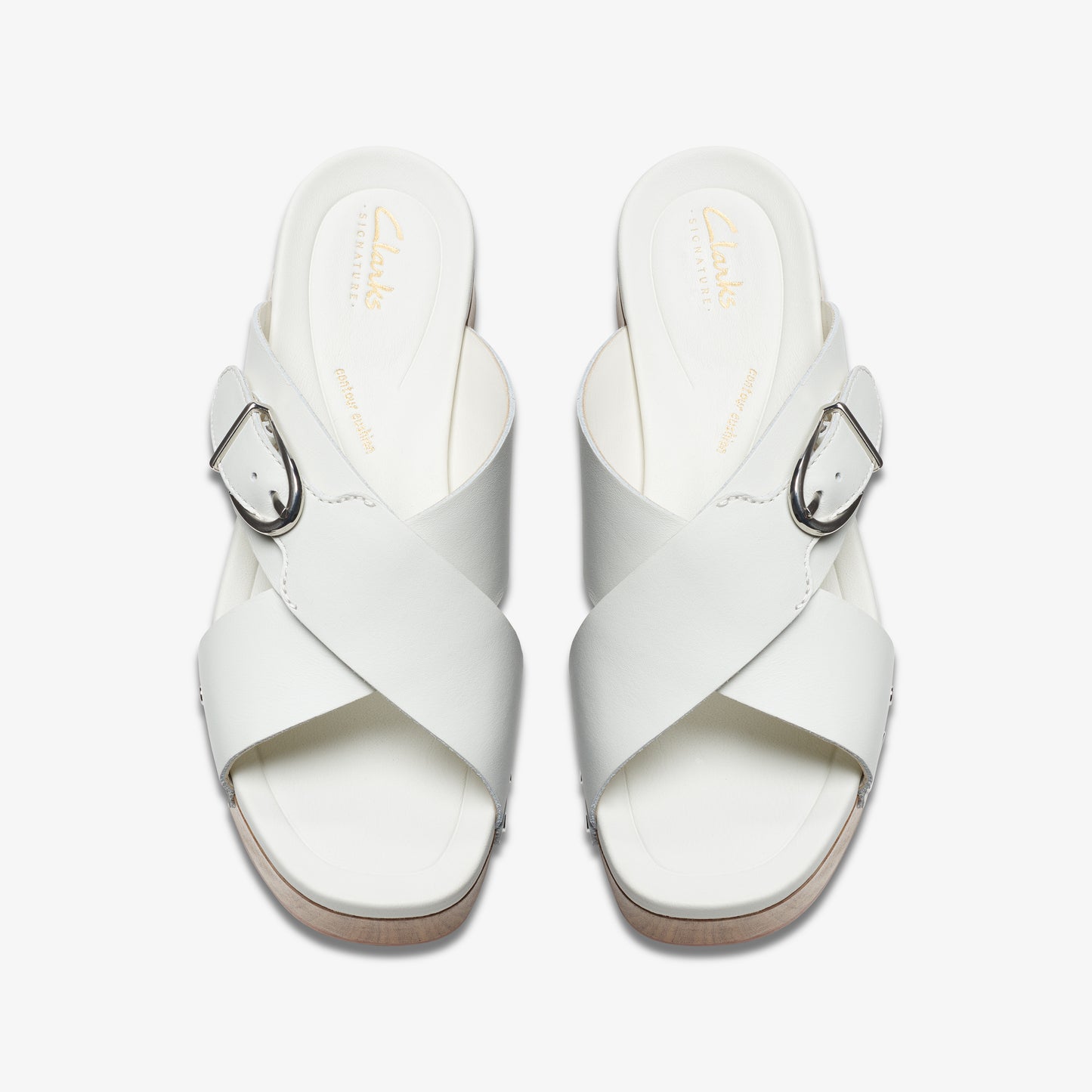 Overhead view of two white leather sandals with cross straps and silver buckles.