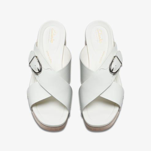 Overhead view of two white leather sandals with cross straps and silver buckles.