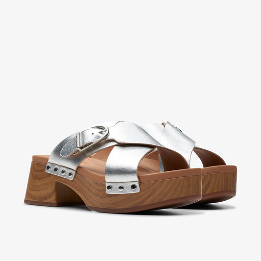 Silver sandal with buckle on wooden platform.