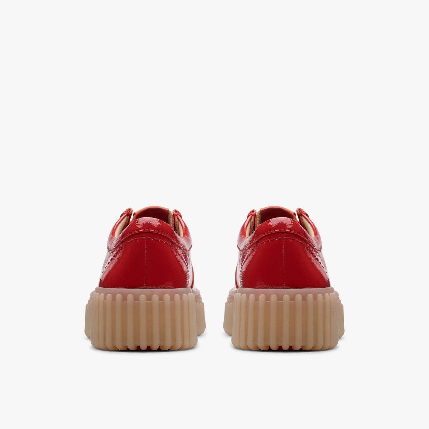 Rear view of two shiny red shoes with thick, tan-colored soles.