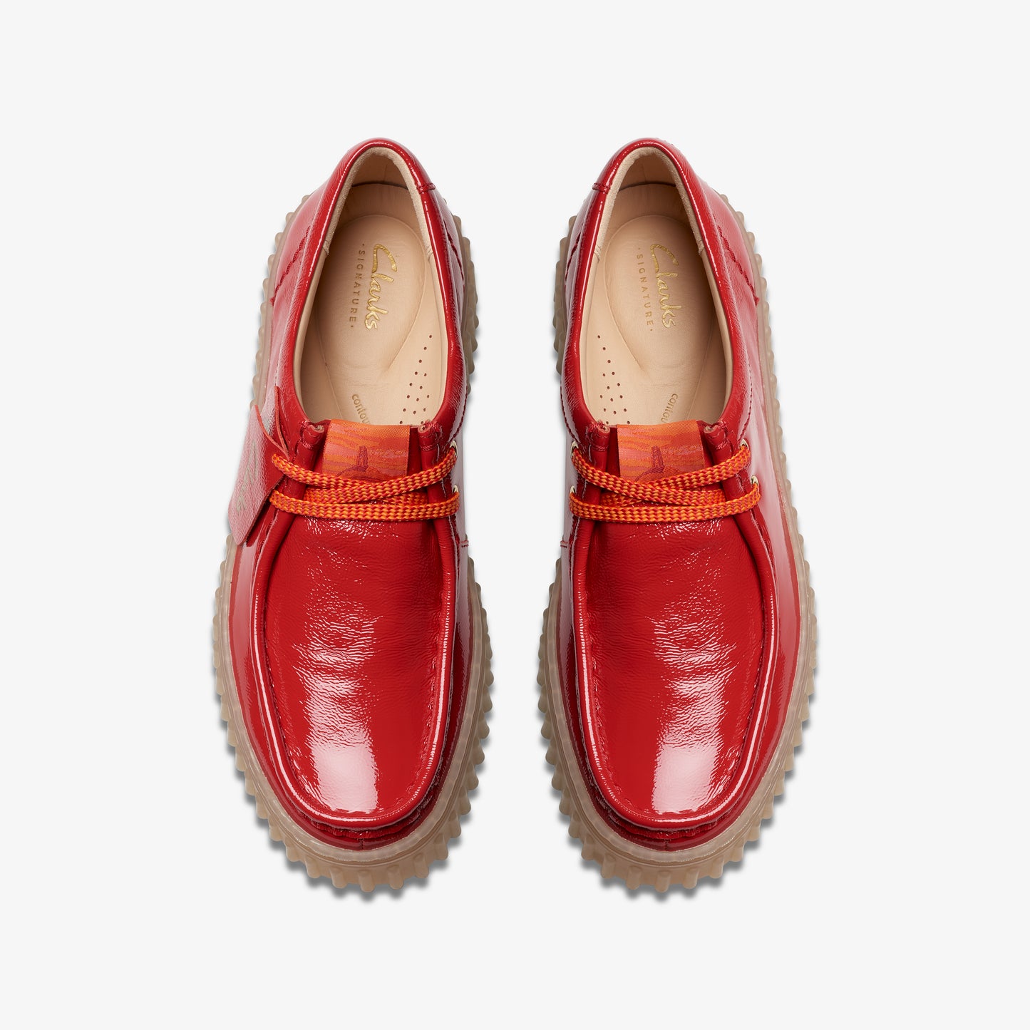 A pair of shiny, red moccasins with orange laces and a textured brown sole, viewed from above.