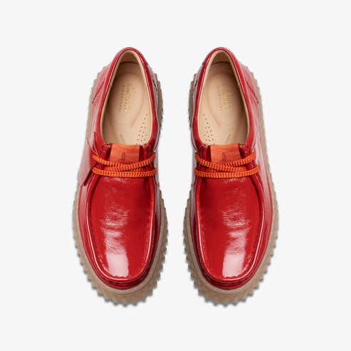 A pair of shiny, red moccasins with orange laces and a textured brown sole, viewed from above.