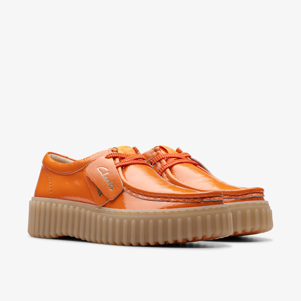Pair of orange patent leather shoes with brown lug soles and orange laces. The label is visible on one shoe.