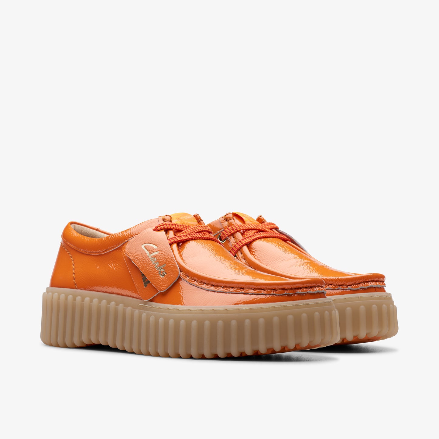 Pair of orange patent leather shoes with brown lug soles and orange laces. The label is visible on one shoe.