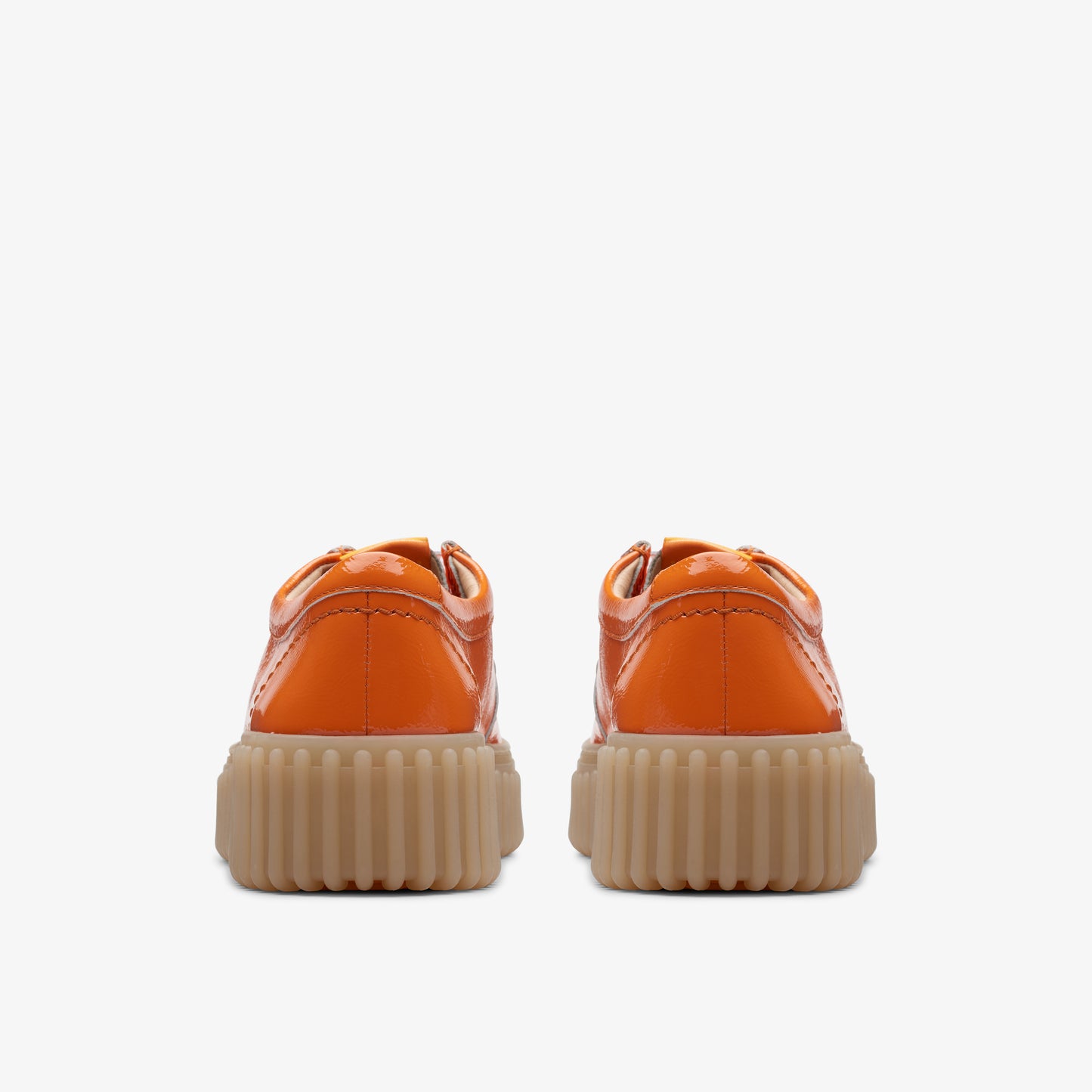 Pair of orange patent leather low top shoes with beige lug soles, seen from the back.