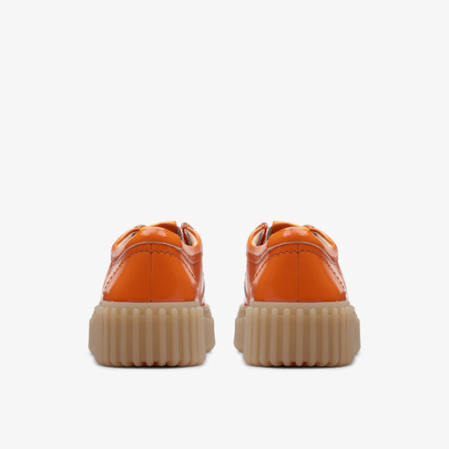 Pair of orange patent leather low top shoes with beige lug soles, seen from the back.