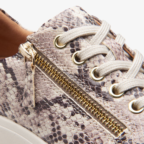 Close-up of a beige snakeskin print sneaker with gold zipper and white laces.