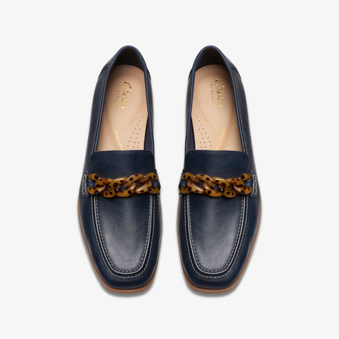 A pair of navy-blue leather loafers, each with a tortoise-shell colored chain detail across the front.