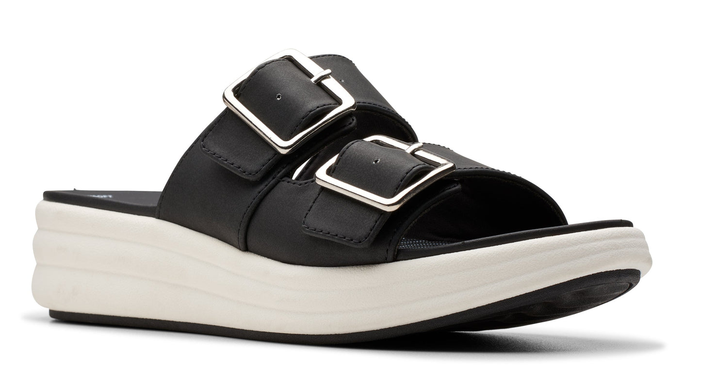 Black slide sandal with two straps, each having a large silver buckle, sitting on a thick white sole.