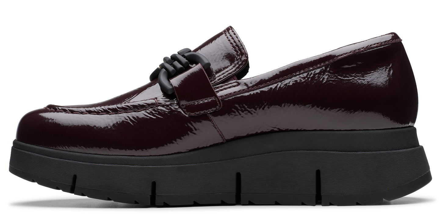 A shiny, dark-burgundy, patent-leather loafer with a black, chunky lug sole and a woven knot detail.