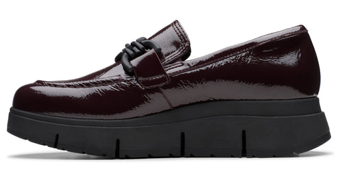 A shiny, dark-burgundy, patent-leather loafer with a black, chunky lug sole and a woven knot detail.