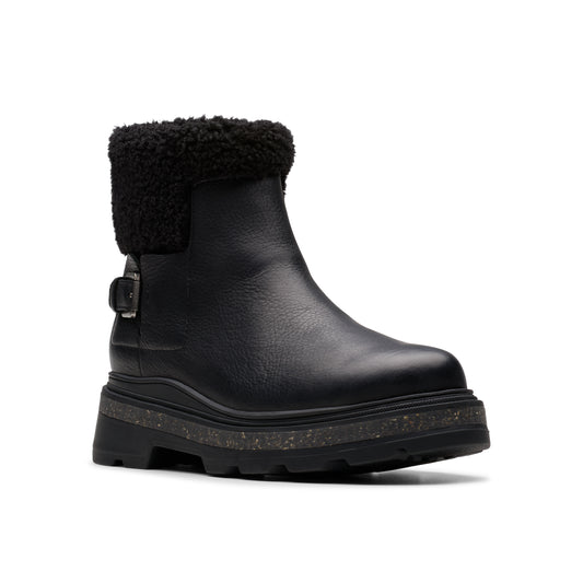 Black leather ankle boot with a black faux-fur collar and buckle detail, atop a chunky lug sole.