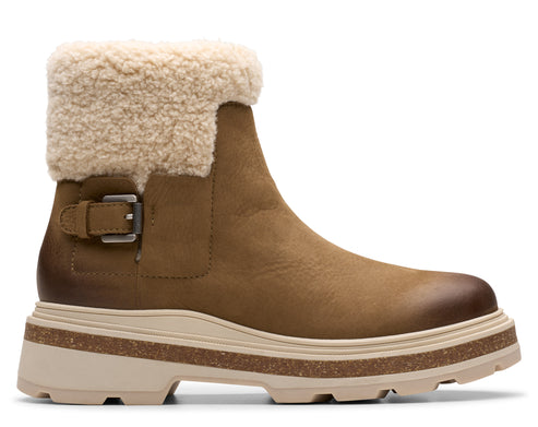 Ankle-high, light brown boot with a fuzzy, light-colored cuff, and a buckled strap near the ankle, resting on a thick, layered sole.