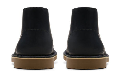 Back view of a pair of leather ankle boots with a dark upper and a tan sole.