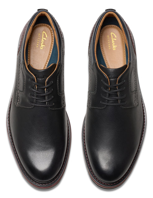 A pair of black leather dress shoes viewed from above, featuring lace-up closures and beige interiors with visible text: Clarks.