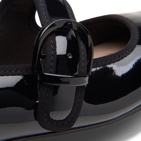 Close-up of a glossy black Mary Jane shoe with a large, round buckle.