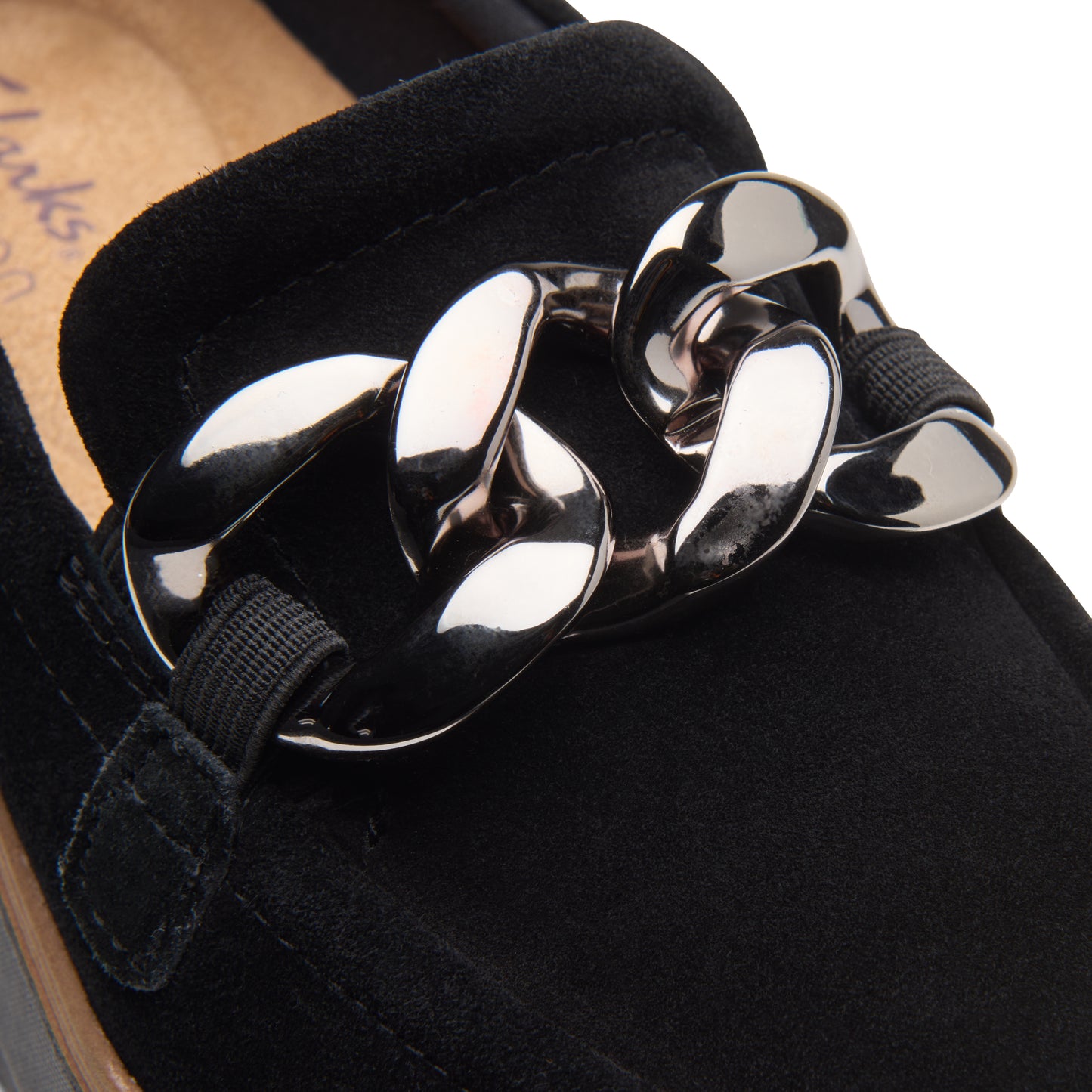 Close-up of black suede loafer with silver chain detail.