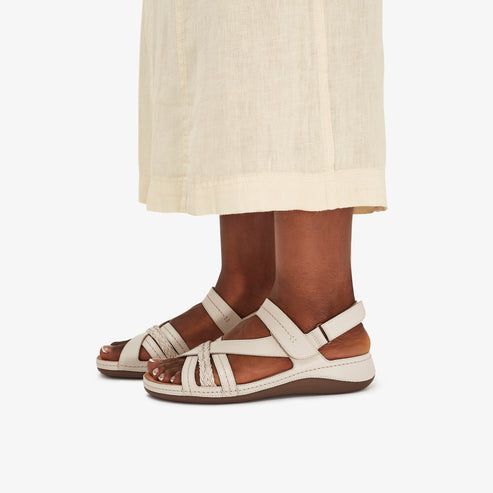A person wearing cream colored sandals with woven straps.