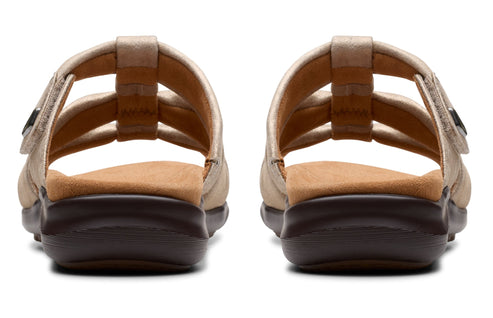 A pair of flat, gold-colored sandals with a dark brown sole, viewed from the back.