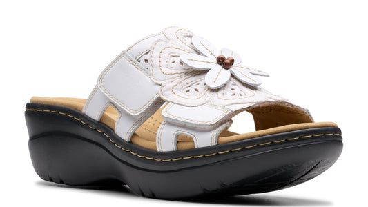 White sandal with flower detail and velcro straps on a wedge sole.