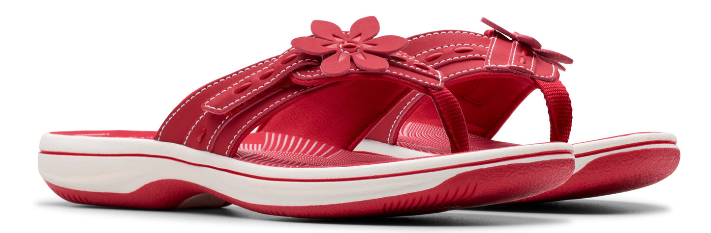 A pair of red sandals with a white sole and a flower embellishment.