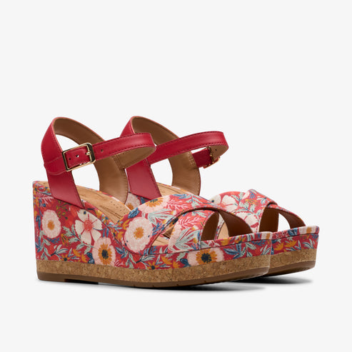 Pair of wedge sandals with floral pattern, red straps and buckle.