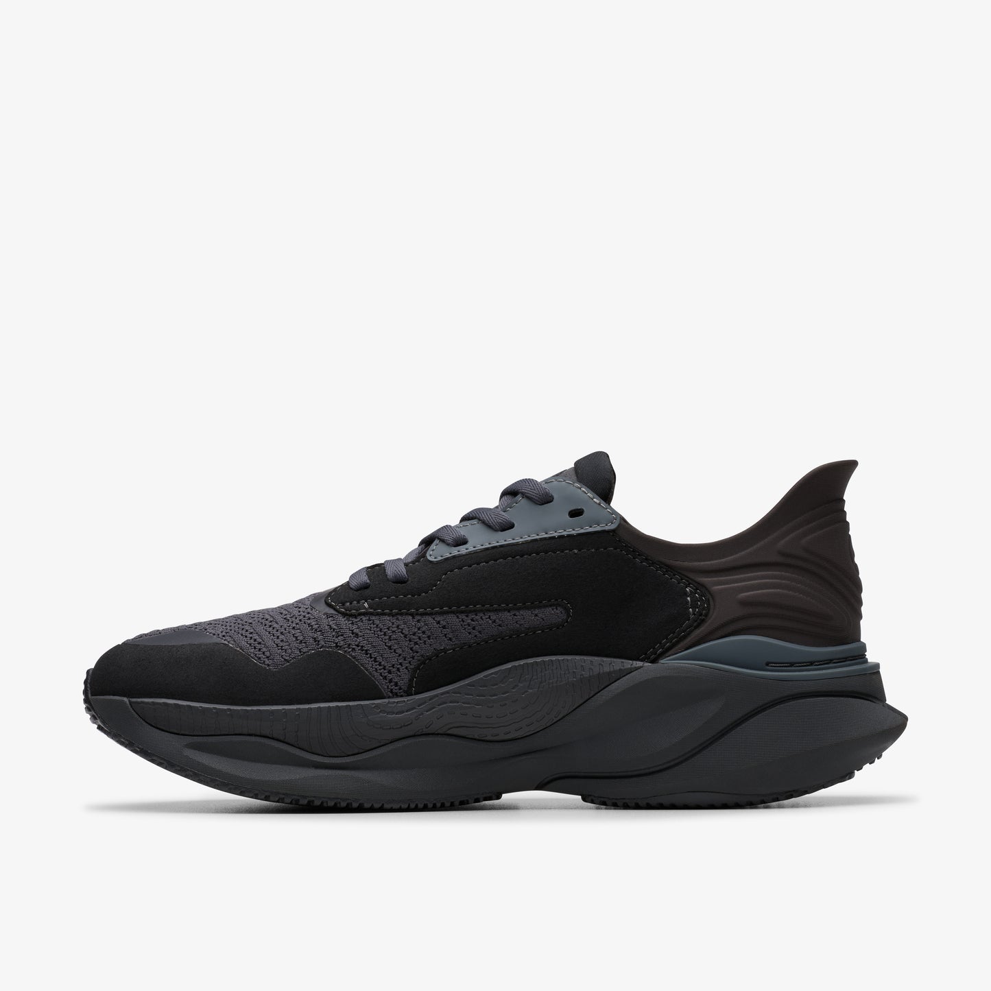 Black running shoe with a wavy sole and a layered upper made of suede and mesh.