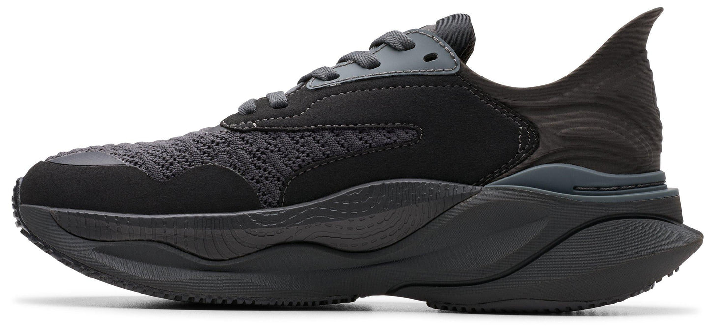 A side-view of a black sneaker with a thick, patterned sole, laces, and a uniquely shaped heel.