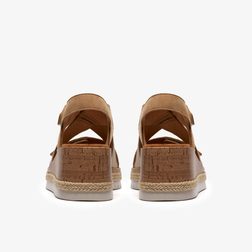 Pair of espadrille wedge sandals with light brown leather, cork platform, and white sole.