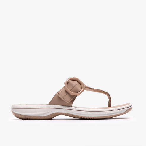 Beige thong sandal with a circular decorative buckle and a white sole.