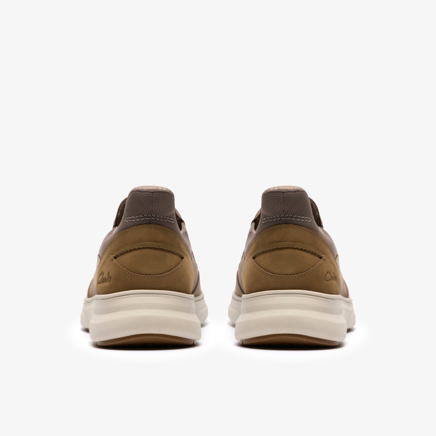 Two casual brown shoes, viewed from behind, displaying their thick, light-colored soles.