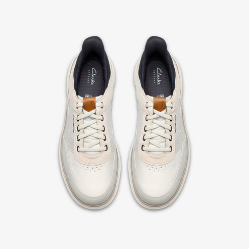Pair of sneakers, top-down view, white with leather laces, dark inner lining and the word "Artisan" on the tongue.