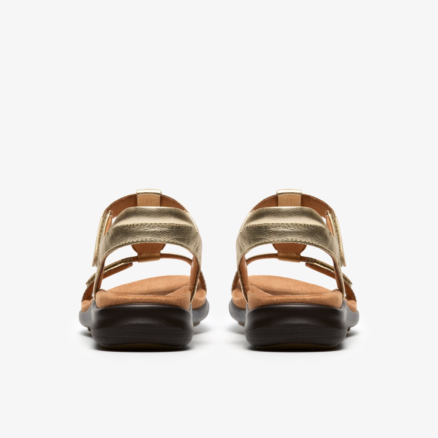 Rear view of gold sandals with adjustable straps and low, dark soles.